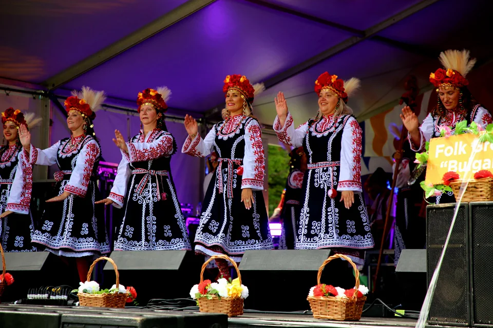 Members of Folk Group "Bulgari" smiling and performing in traditional embroidered folk attire on stage at the 2025 National Multicultural Festival in Canberra.